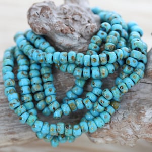 May include: A strand of turquoise blue glass beads with gold flecks. The beads are small and round, and they are strung together on a clear thread.