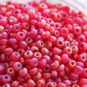 Könnte beinhalten: Nahaufnahme eines Stapels kleiner, runder, irisierender rosa Perlen. Die Perlen haben eine glatte, glänzende Oberfläche und sind perfekt für die Schmuckherstellung.