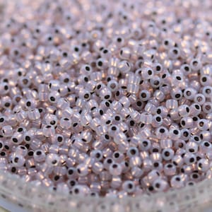 May include: A close-up view of a large quantity of small, round, iridescent white beads with black centers. The beads are arranged in a random pattern and appear to be made of glass.