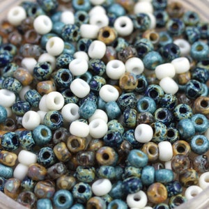 May include: A close-up of a variety of small, round beads. The beads are a mix of white, brown, and blue colors. The beads are all about the same size and are arranged in a random pattern.