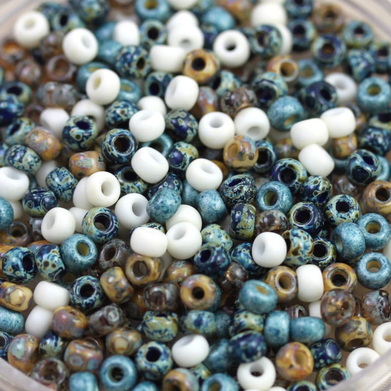 May include: A close-up of a variety of small, round beads. The beads are a mix of white, brown, and blue colors. The beads are all about the same size and are arranged in a random pattern.
