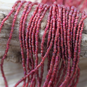 May include: A strand of red iridescent seed beads. The beads are small and round, and they have a subtle shimmer to them.