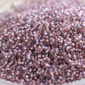 Puede incluir: Primer plano de un montón de pequeñas cuentas de semillas de color púrpura iridiscente. Las cuentas son redondas y tienen una apariencia ligeramente translúcida.