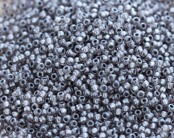 May include: A close-up view of a large quantity of small, round, silver-colored glass beads. The beads have a slightly iridescent finish and are perfect for jewelry making or other craft projects.