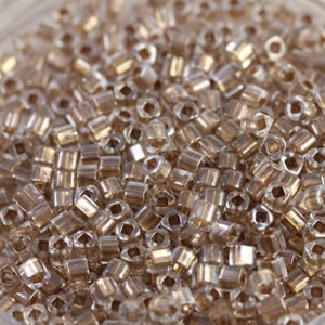 May include: A close-up of a large quantity of small, clear glass beads with a gold iridescent finish. The beads are in a round container.