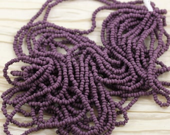 May include: A strand of small, round, matte purple beads. The beads are strung together on a white thread.