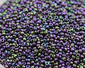 May include: A close-up view of a large quantity of small, round, iridescent beads. The beads are a mix of dark purple and green colors with a metallic sheen.
