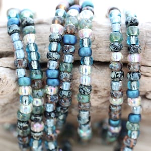 May include: A close-up of a strand of blue, silver, and black seed beads. The beads are arranged in a circular pattern and are strung on a clear thread.