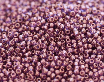 May include: A close-up view of a large quantity of small, round, metallic purple beads. The beads have a shiny, iridescent finish.