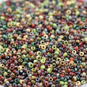 May include: A large assortment of small, colourful glass beads in shades of green, brown, red, and cream. The beads are all approximately the same size and are arranged in a random pattern.