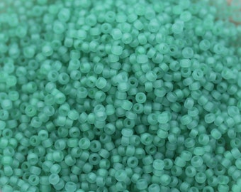 May include: A close-up view of a large quantity of small, round, opaque, light green glass beads. The beads are all the same size and shape, and they are arranged in a random pattern.