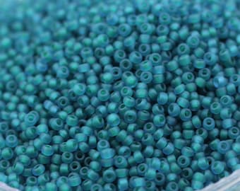 May include: A close-up view of a large quantity of teal blue seed beads. The beads are small and round, with a matte finish.