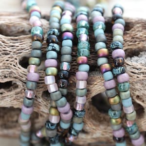 May include: A close-up of a strand of beads in various shades of green, brown, and purple. The beads are arranged in a circular pattern and are made of glass.