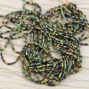 May include: A collection of small, square beads in green, brown, yellow, and blue. The beads are strung together, forming a textured and colourful display. These beads are likely for jewellery making.