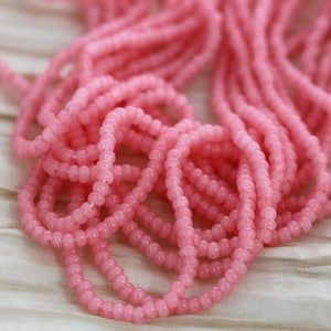 May include: A close-up of a pile of pink seed beads. The beads are small and round, and they are arranged in a random pattern.