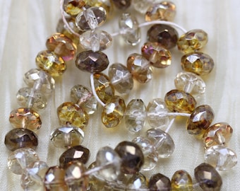May include: A strand of faceted glass beads in shades of brown, yellow, and clear. The beads are strung on a white thread and have a faceted, teardrop shape.