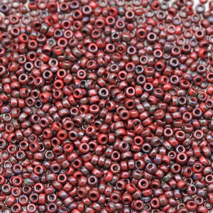 May include: A close-up image of a large quantity of small, red, round seed beads. The beads have a speckled, iridescent finish.