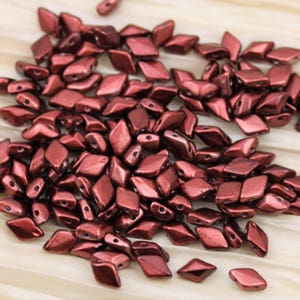 May include: A pile of small, dark red, faceted glass beads. The beads are shaped like diamonds and have a metallic sheen.