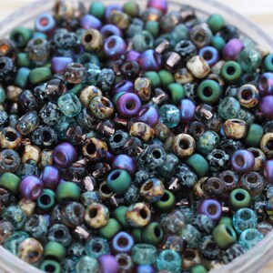 K&ouml;nnte beinhalten: Eine Mischung aus kleinen, bunten Glasperlen in den Farben T&uuml;rkis, Gr&uuml;n, Lila und Braun. Die Perlen haben verschiedene Oberfl&auml;chen, darunter irisierend, matt und gesprenkelt.
