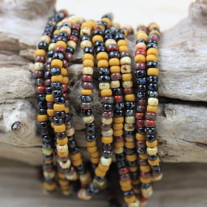 May include: A strand of colorful seed beads in shades of black, red, yellow, and white. The beads are small and round, and they are strung together on a clear thread.