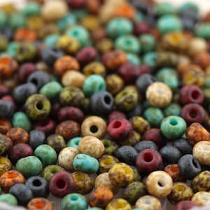 May include: A collection of small, round, rustic beads in a variety of earthy colours including turquoise, terracotta, olive green, charcoal grey, and cream. Each bead features a speckled, matte finish and a central hole for threading.