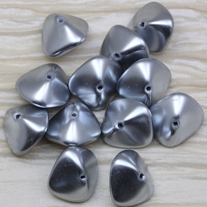 May include: A group of 12 silver-colored, iridescent, plastic beads. The beads are shaped like a flower petal with a hole in the center.