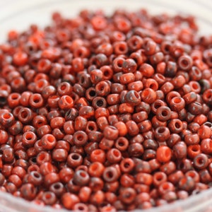 Könnte beinhalten: Nahaufnahme einer großen Menge kleiner, runder Perlen in Rot- und Brauntönen. Die Perlen haben eine gesprenkelte, marmorierte Optik.