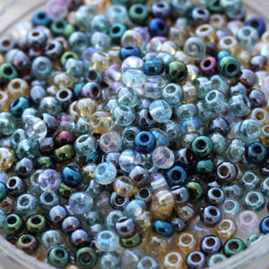 May include: A close-up of a collection of small, transparent beads. The beads are a mix of colours, including blue, green, purple, and gold. They appear to be made of glass or a similar material, and are likely used for jewellery making or crafts.