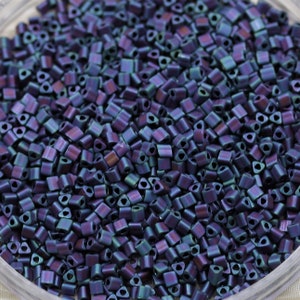 May include: A close-up view of a container filled with small, iridescent, dark blue and purple triangle-shaped beads.