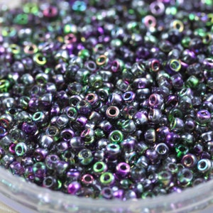 May include: A close-up of a large quantity of iridescent seed beads in shades of purple, green, and black.