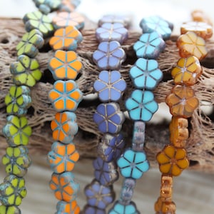May include: Five strands of flower-shaped glass beads in various colors, including turquoise, orange, purple, and yellow. The beads are strung on a wire and are arranged in a row.