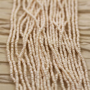 May include: Close-up of multiple strands of small, off-white pearls. The strands are arranged vertically, creating a cascading effect. The pearls have a subtle lustre and are set against a soft, neutral-toned background, suggesting a jewelry or craft supply.