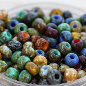 May include: A close-up of a bowl filled with colorful glass beads. The beads are small and round, with a variety of patterns and colors, including brown, green, blue, and red.