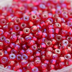 May include: A close-up view of a large quantity of small, round, red glass beads with a silver iridescent sheen.