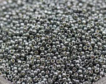 May include: A close-up view of a large quantity of silver seed beads. The beads are small and round, with a metallic sheen.