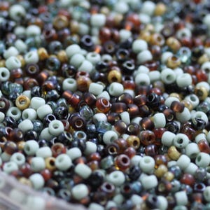May include: A close-up shot of a collection of small, round beads in shades of brown, beige, grey, and black. The beads are arranged in a random pattern, creating a visually appealing texture.