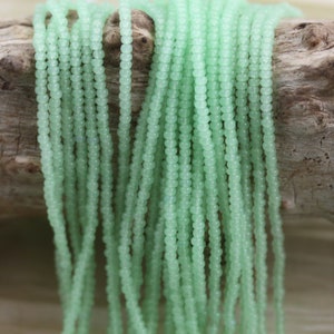 May include: A strand of light green glass beads, each bead is round and slightly translucent. The beads are strung on a thin wire and are arranged in a loose pile.