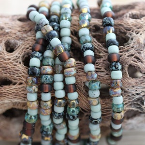 May include: A close-up of a strand of multi-coloured beads. The beads are a mix of light blue, brown, black, and gold. The beads are arranged in a random pattern.