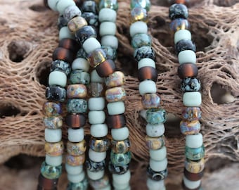 May include: A close-up of a strand of multi-colored beads. The beads are a mix of light blue, brown, black, and gold. The beads are arranged in a random pattern.