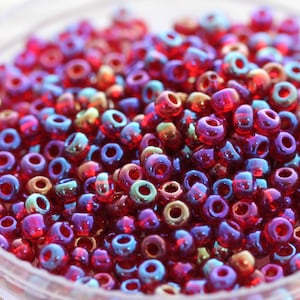 May include: A close-up of a large quantity of small, round, iridescent red glass beads. The beads have a metallic sheen and are perfect for jewelry making or crafting.