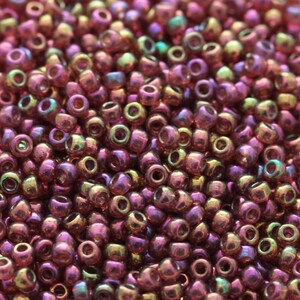 May include: A close-up shot of a collection of small, shimmering beads. The beads are predominantly pink and purple, with touches of gold and green. These beads are suitable for jewellery making or other craft projects.