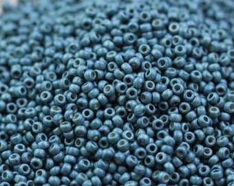 May include: A close-up view of a large quantity of small, round, teal-colored beads. The beads have a slightly metallic sheen and are arranged in a random pattern.