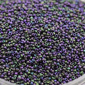 May include: A close-up view of a large quantity of small, round, iridescent beads. The beads are a mix of purple and green colors with a metallic sheen.