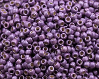 May include: A close-up image of a large quantity of small, round, purple beads. The beads have a metallic sheen and are arranged in a random pattern.