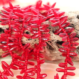 Op de afbeelding: Een streng helderrode glazen kralen in bladvorm. De kralen zijn aan elkaar geregen op een doorzichtige draad.