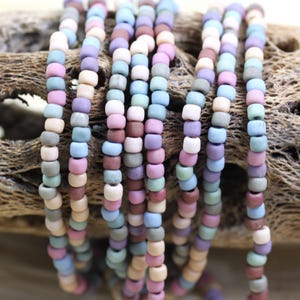 May include: A strand of small, colorful glass beads in shades of blue, green, pink, brown, and white. The beads are arranged in a random pattern and are strung on a clear thread.