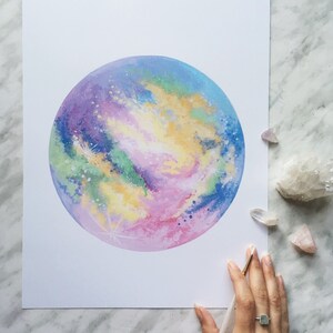 Pu&ograve; includere: Un dipinto ad acquerello di una galassia colorata con sfumature di rosa, viola, blu, verde e giallo. La galassia &egrave; dipinta in una forma circolare, che ricorda un pianeta.