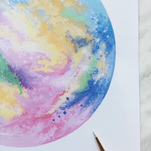 Pu&ograve; includere: Un dipinto ad acquerello di una galassia colorata con sfumature di blu, rosa, giallo e verde. La galassia &egrave; dipinta in forma circolare e ha uno sfondo bianco.