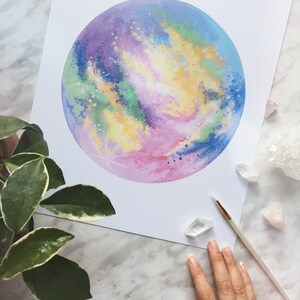 Pu&ograve; includere: Un dipinto ad acquerello di una galassia colorata con sfumature di rosa, blu, verde e giallo. La galassia &egrave; dipinta in forma circolare e sembra brillare.