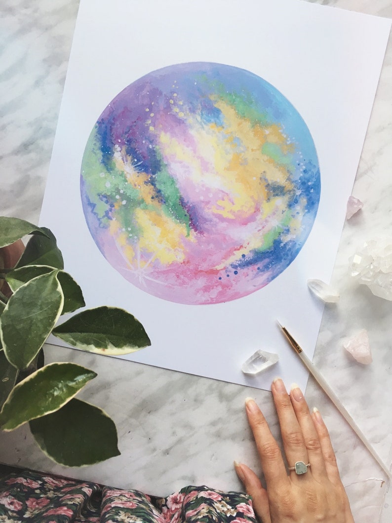 Pu&ograve; includere: Un dipinto ad acquerello di una galassia colorata con sfumature di rosa, blu, verde e giallo. La galassia &egrave; dipinta in forma circolare e sembra brillare.